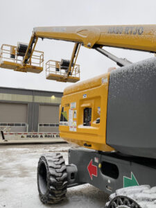 A boom lift with Hugg & Hall stickers in winter weather. The tires and top of the machinery are dusted with snow. 