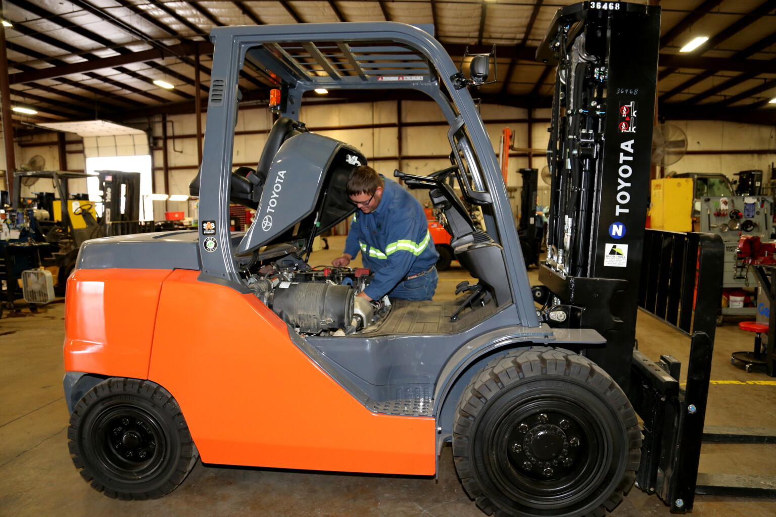 A technician in a blue uniform performs maintenance on an orange Toyota forklift. Article: How to Dispose of Used Oil.