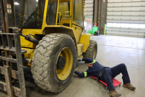 A technician in a blue uniform performs maintenance on a forklift. Article: How to Dispose of Used Oil.