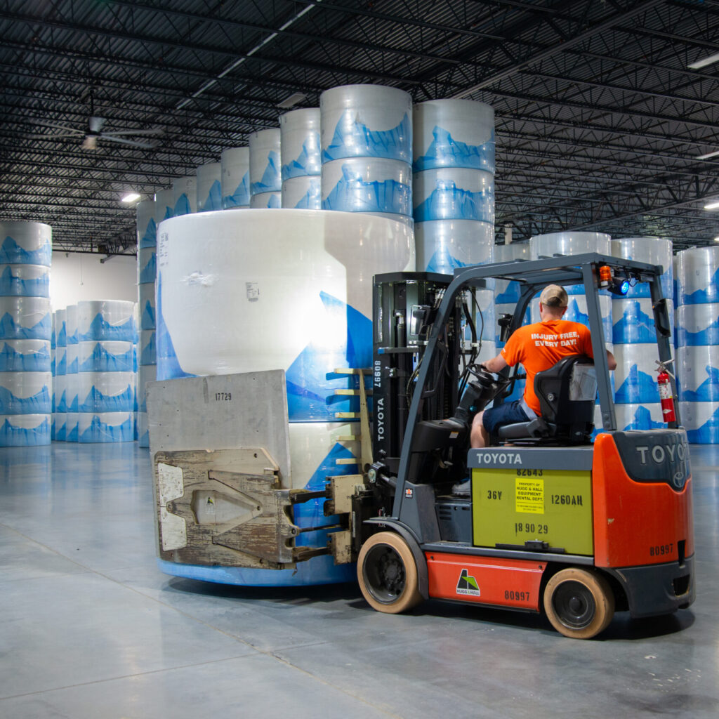 A Hugg & Hall Toyota Forklift with a clamp forklift attachment type. The clamp is holding a large roll of paper. 