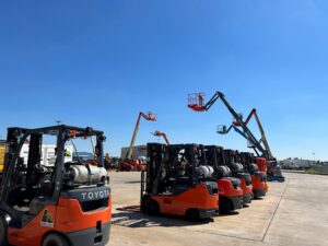 Toyota branded forklifts and boom lifts in background of a yard on a cloudless day